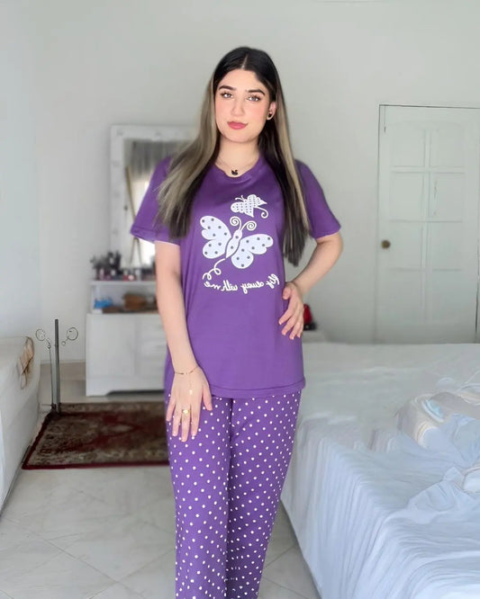 Woman wearing a purple pajama set with a white butterfly design in a bedroom.
