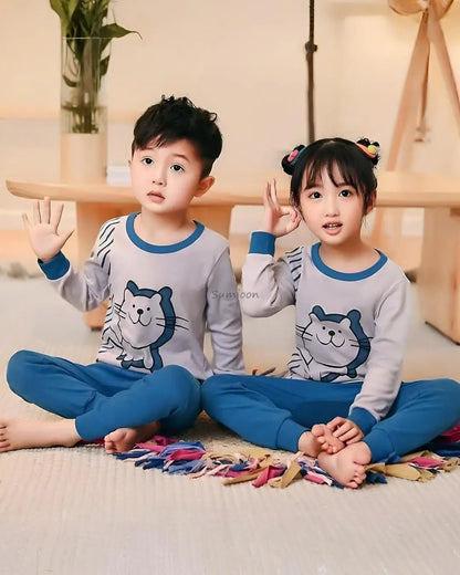 A young boy and girl sitting together, wearing matching grey and blue kids' full-sleeve cartoon suits with a cat character print.