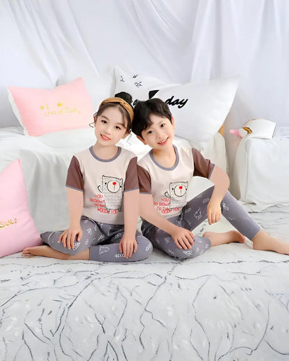 A young child wearing a half-sleeved grey suit with a kitty print on the t-shirt, standing and smiling.