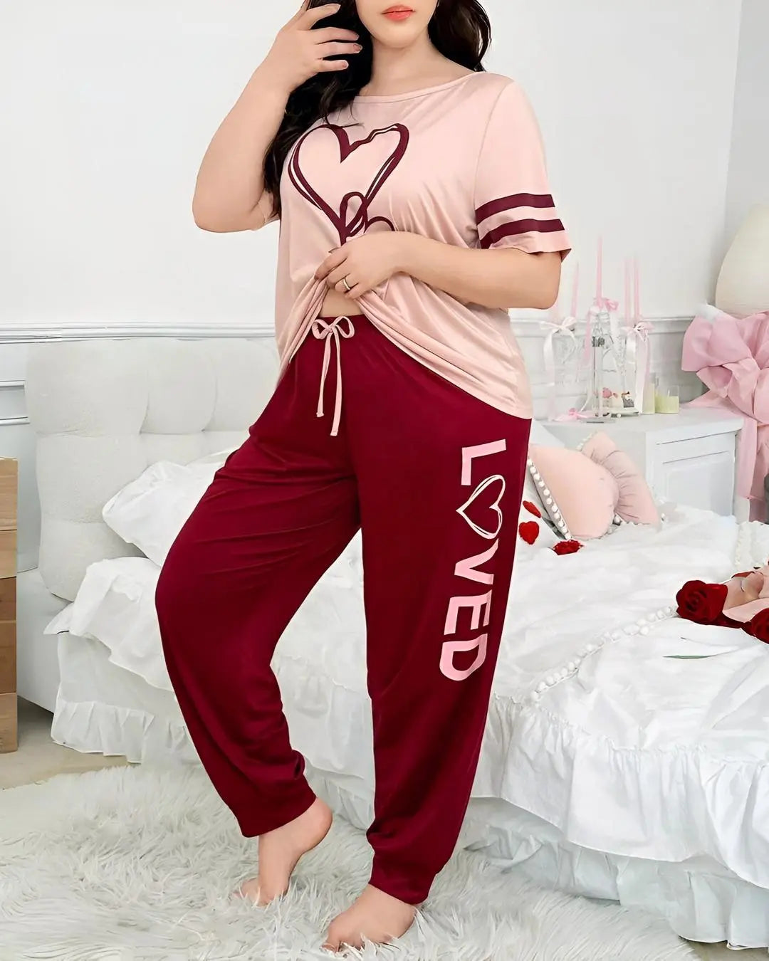 A women wearing a two-piece pajama set with a pale pink top and maroon pants. The top has a heart print, and the pants have "LOVED" printed on them.