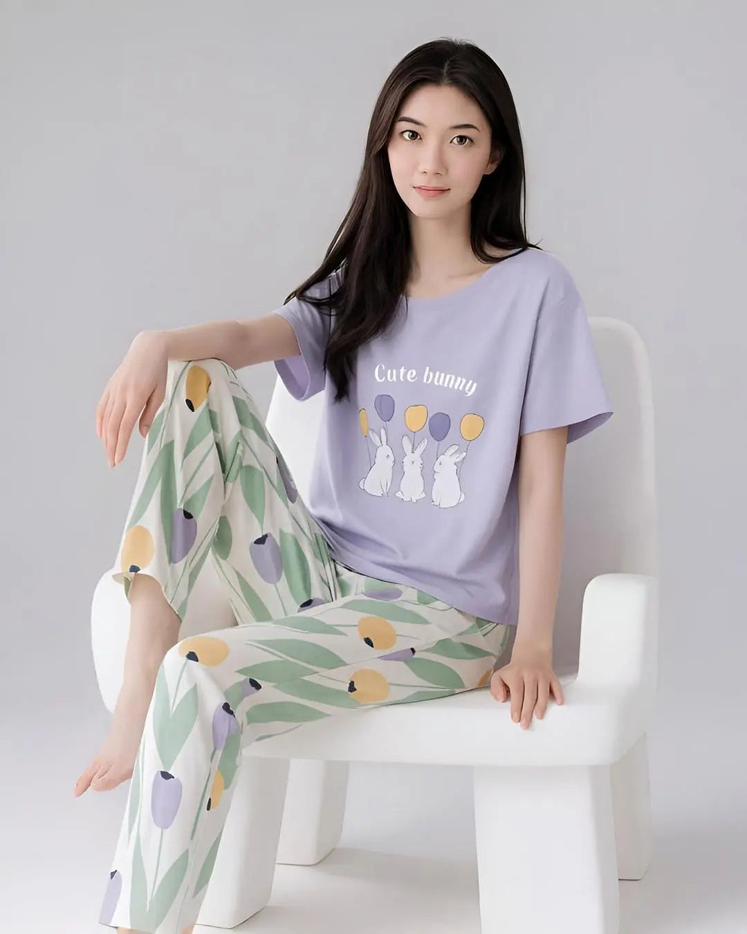 Woman wearing a purple t-shirt with 'Cute bunny' text and patterned pants sitting on a white chair.