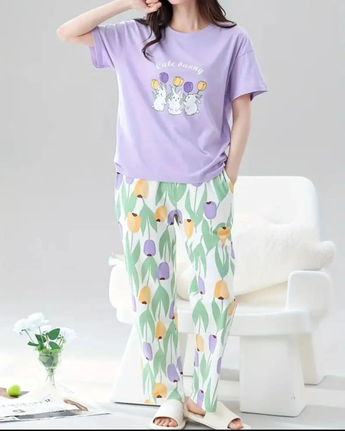 A person wearing a purple t-shirt and patterned pants sitting on a white chair.